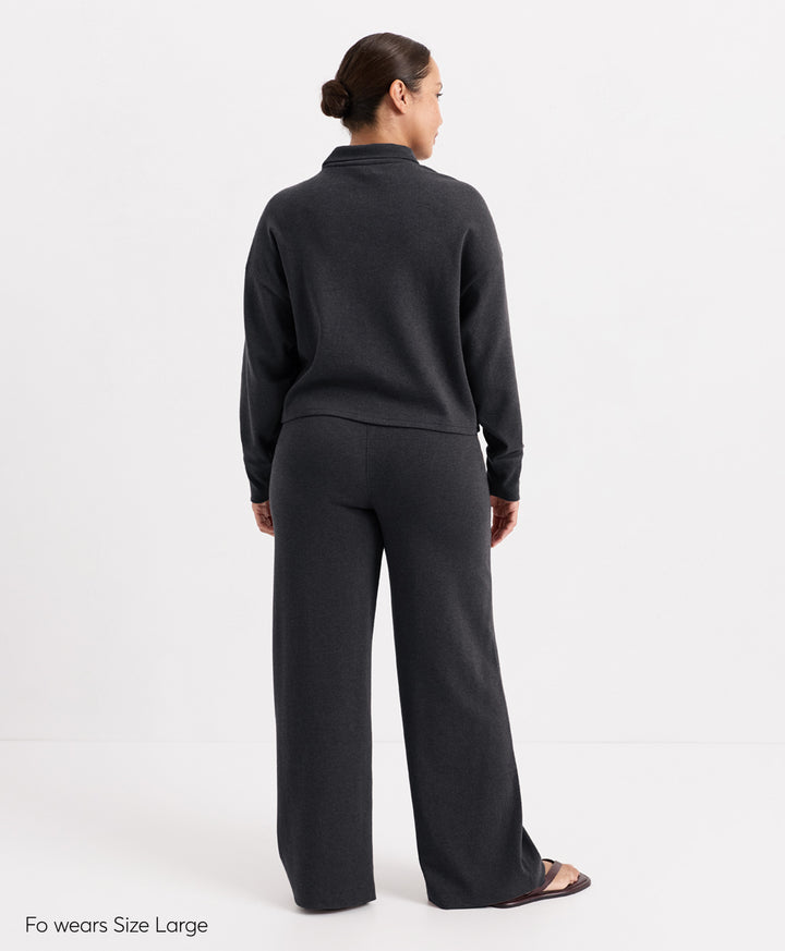 A model shown from the back wearing a dark charcoal heather mock-neck long-sleeve top and matching wide-leg trousers, photographed against a clean white studio background.