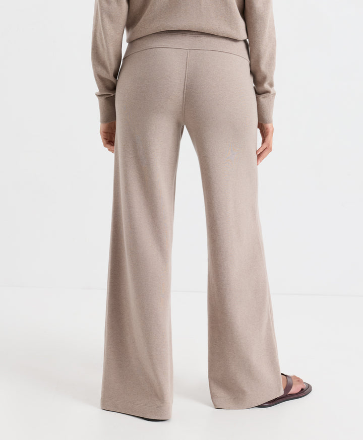A person shown from the back wearing a light taupe knit sweater and matching wide-leg trousers, photographed against a clean white studio background.