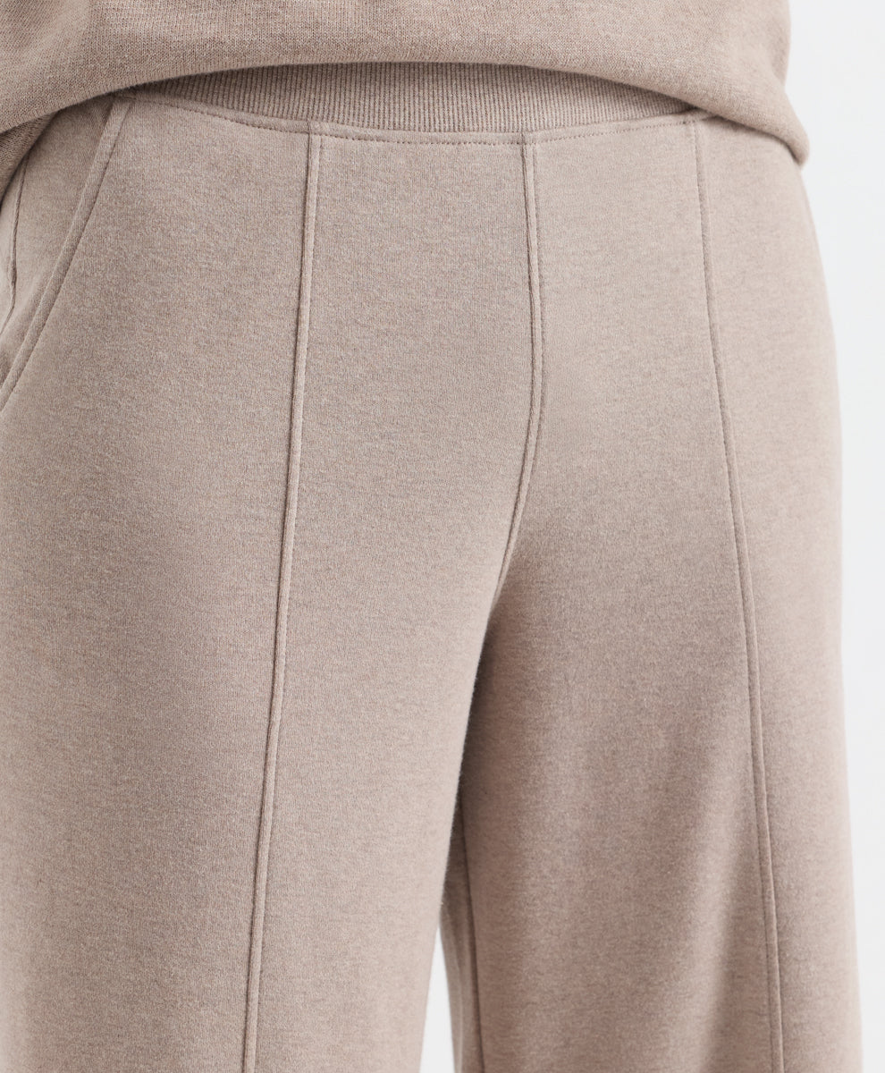 Close-up of a person wearing light taupe-beige knit pants with a ribbed waistband and front seam detailing, paired with a matching top.