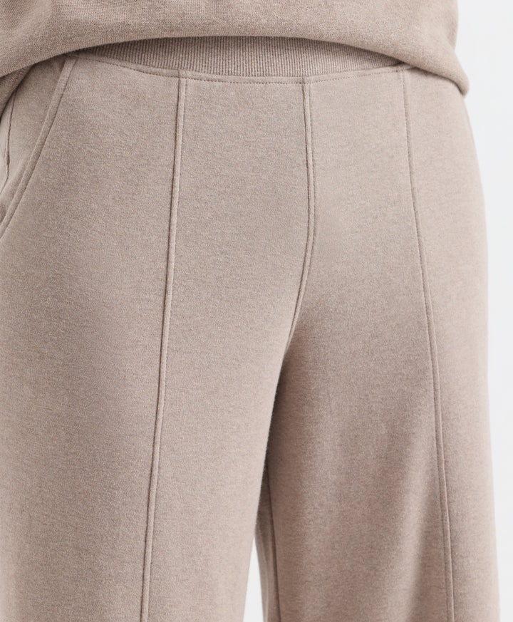 Close-up of a person wearing light taupe-beige knit pants with a ribbed waistband and front seam detailing, paired with a matching top.
