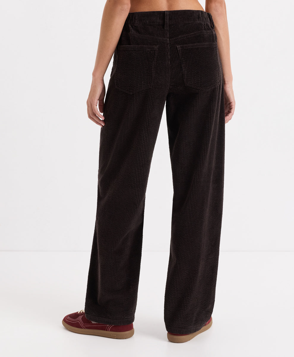 A person shown from the back wearing espresso corduroy barrel pants and burgundy slip-on shoes against a clean white studio background.