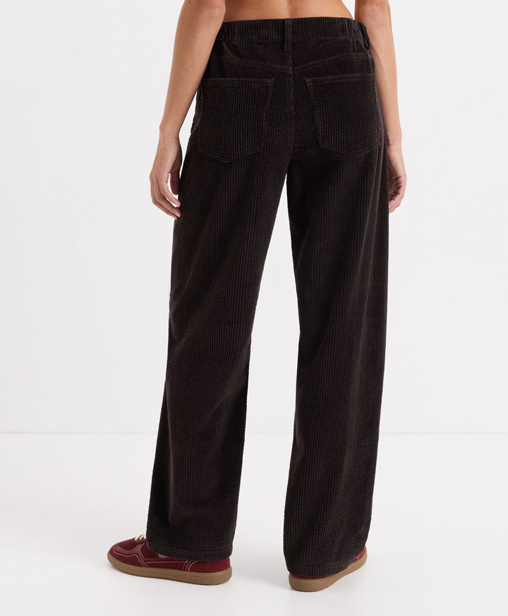 A person shown from the back wearing espresso corduroy barrel pants and burgundy slip-on shoes against a clean white studio background.