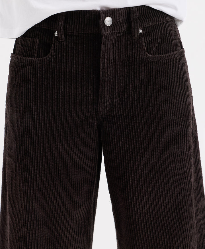 Close-up of espresso corduroy barrel pants with a white shirt hem visible at the top, showing the front waistband, button, belt loops, and side pockets.