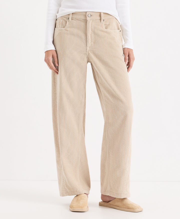 A person wearing parchment barrel corduroy pants, styled with a white long-sleeve top and beige slip-on shoes, photographed against a clean white studio background.