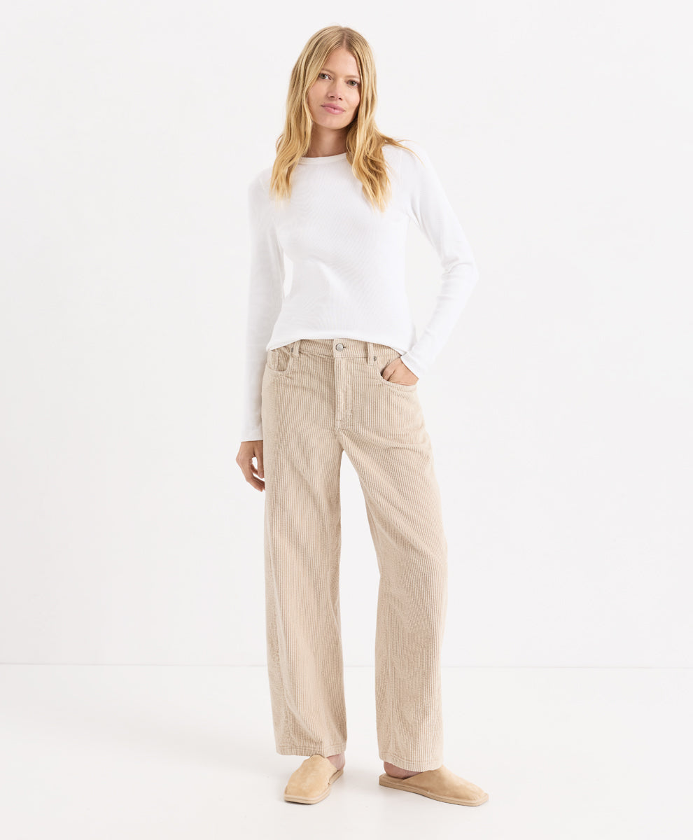 A woman modeling a white long-sleeve knit top and parchment corduroy barrel pants, paired with beige slip-on shoes, against a clean white studio background.