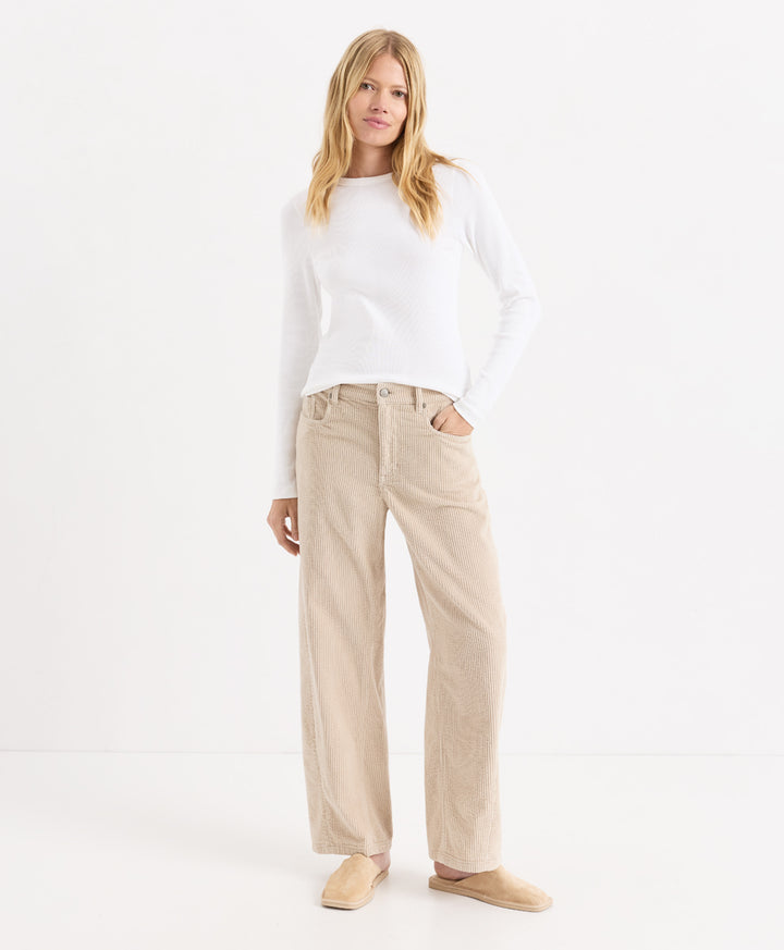 A woman modeling a white long-sleeve knit top and parchment corduroy barrel pants, paired with beige slip-on shoes, against a clean white studio background.