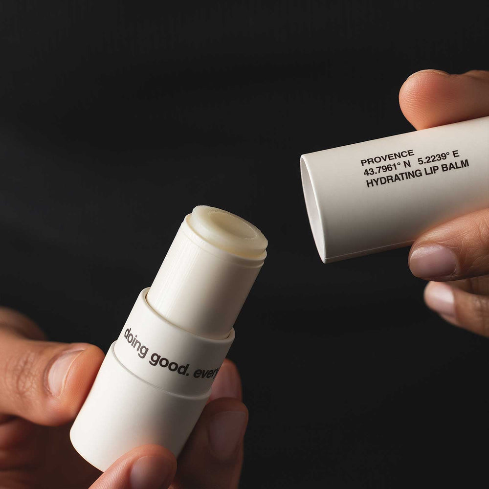 Open lip balm products held by hands against a black background