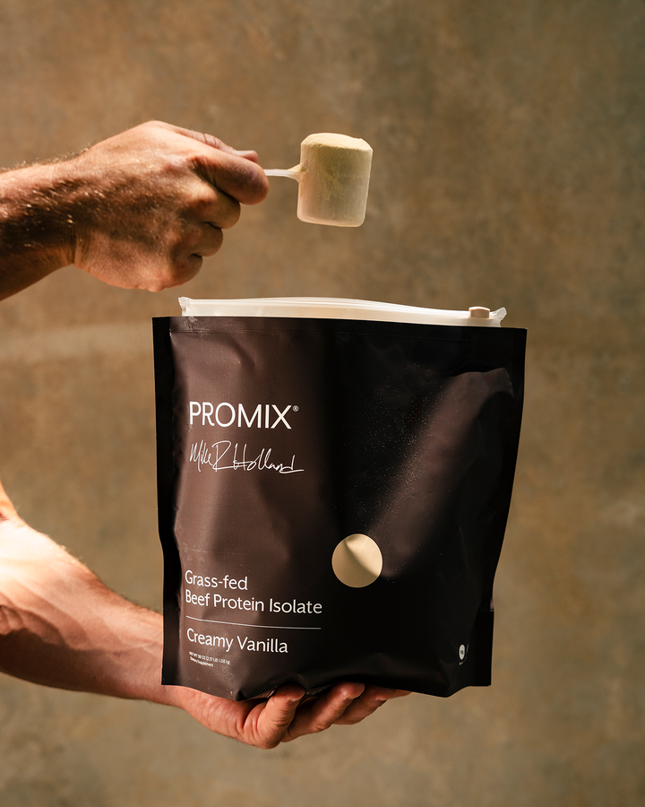 A person holds a brown PROMIX protein powder bag while pouring a scoop of creamy vanilla protein powder from a scoop above the bag, against a warm, textured brown background.