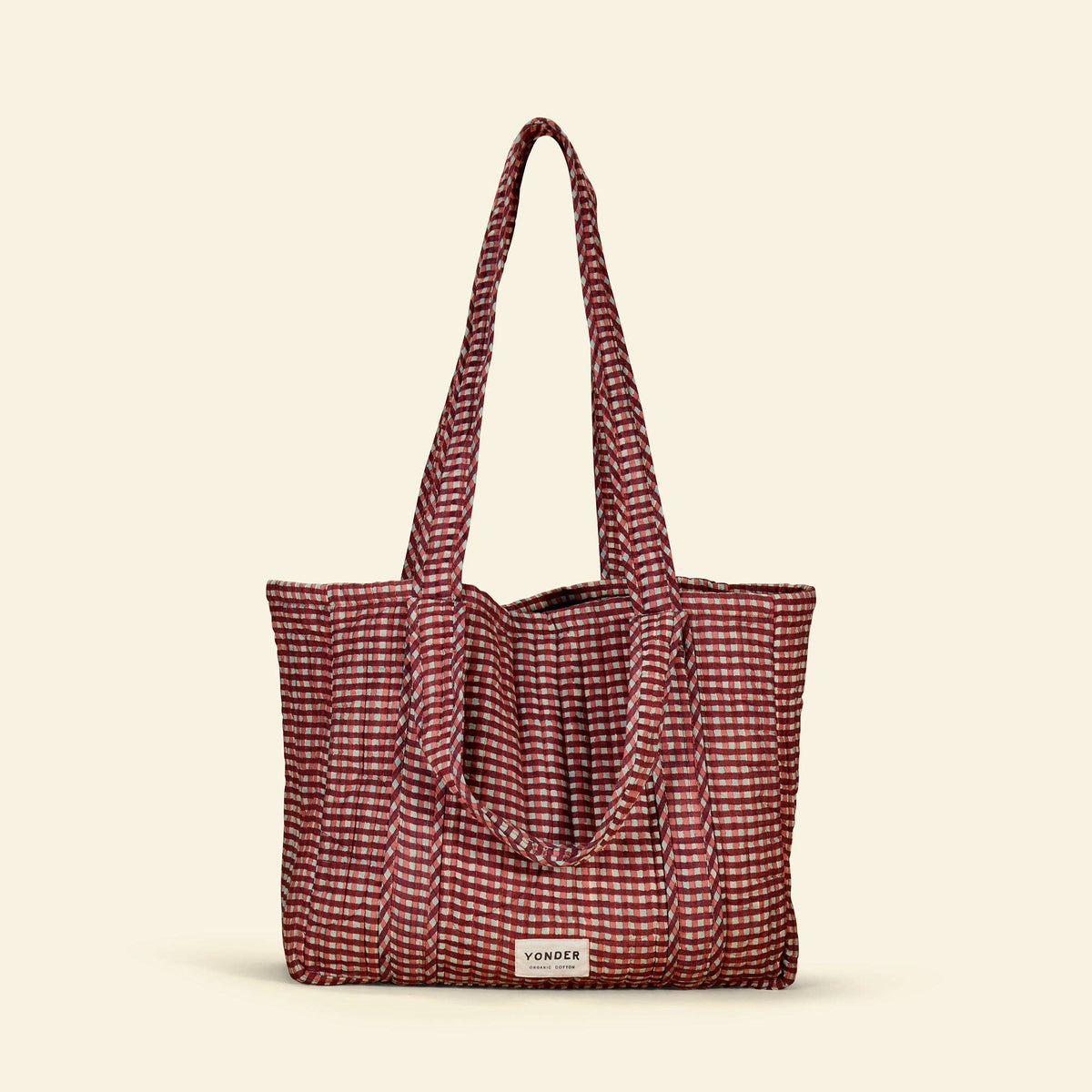 A red and white gingham patterned tote bag with long shoulder straps, shown against a solid cream background. A small white brand label reading 'YONDER' is visible on the front.