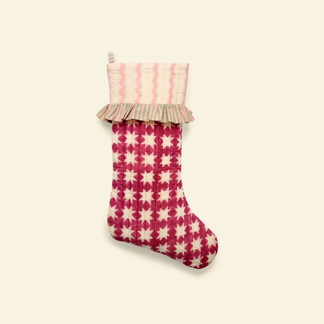 A quilted Christmas stocking with a pink and cream star pattern body, a striped ruffled cuff, and a hanging loop, shown against a solid cream background.