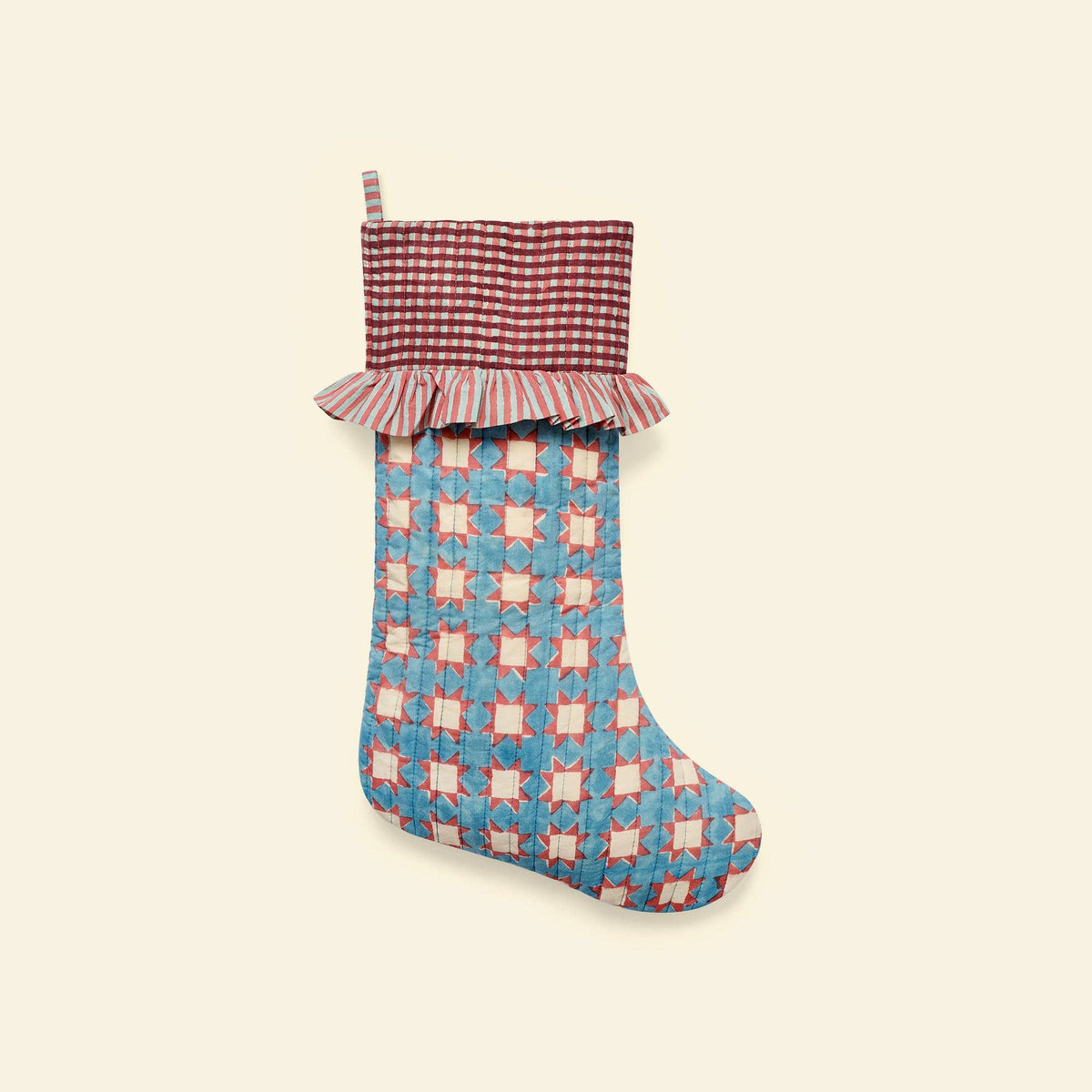 A vintage-style quilted Christmas stocking with a blue and red starburst pattern body, a red and white gingham patterned cuff with a ruffled edge, and a hanging loop, shown against a solid cream background.