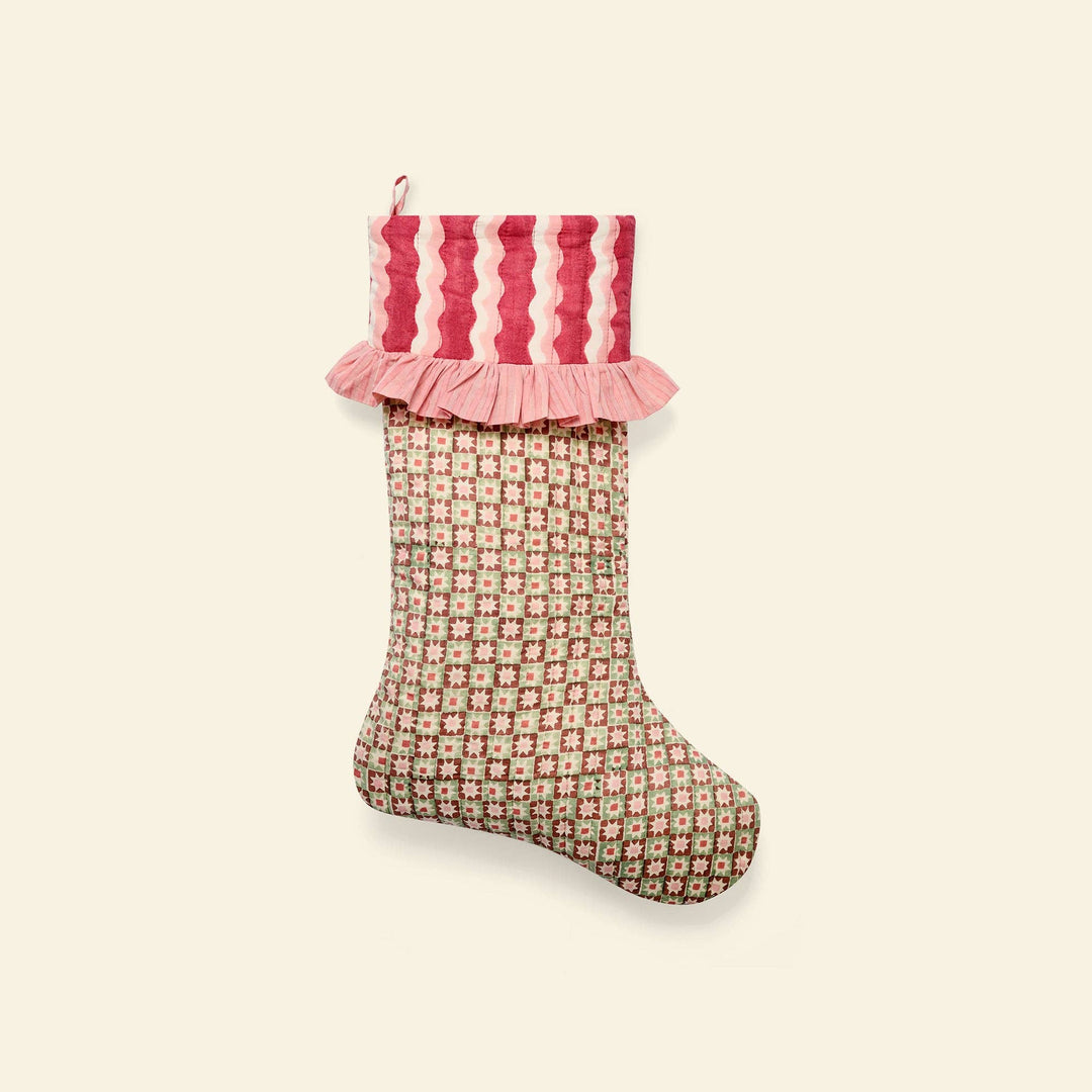 A Christmas stocking with a pink and red striped ruffled cuff and a beige, pink, and red floral patterned body, shown against a solid cream background.