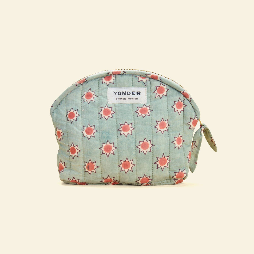 A quilted cosmetic pouch in light blue cotton with a repeating coral-pink starburst pattern, featuring a white Yonder brand label on the front.