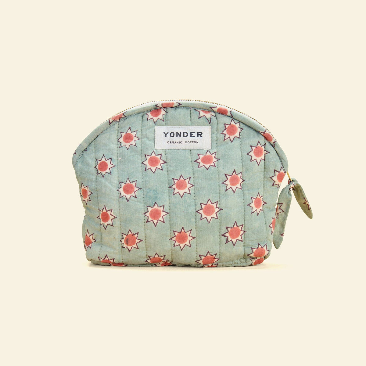 A quilted cosmetic pouch in light blue cotton with a repeating coral-pink starburst pattern, featuring a white Yonder brand label on the front.