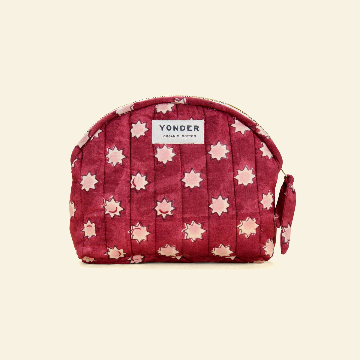 A quilted cosmetic pouch in deep burgundy with a pink and white star pattern, featuring a white label that reads 'YONDER CORKSEED COTTON'.