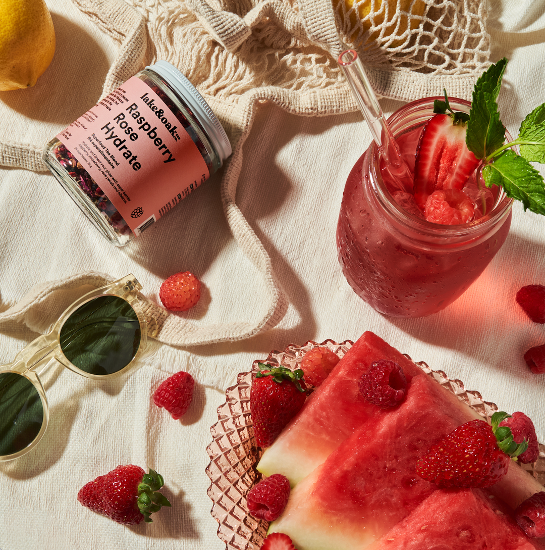 Pink drink with strawberries, watermelon, and a jar of pink tea on a light surface.