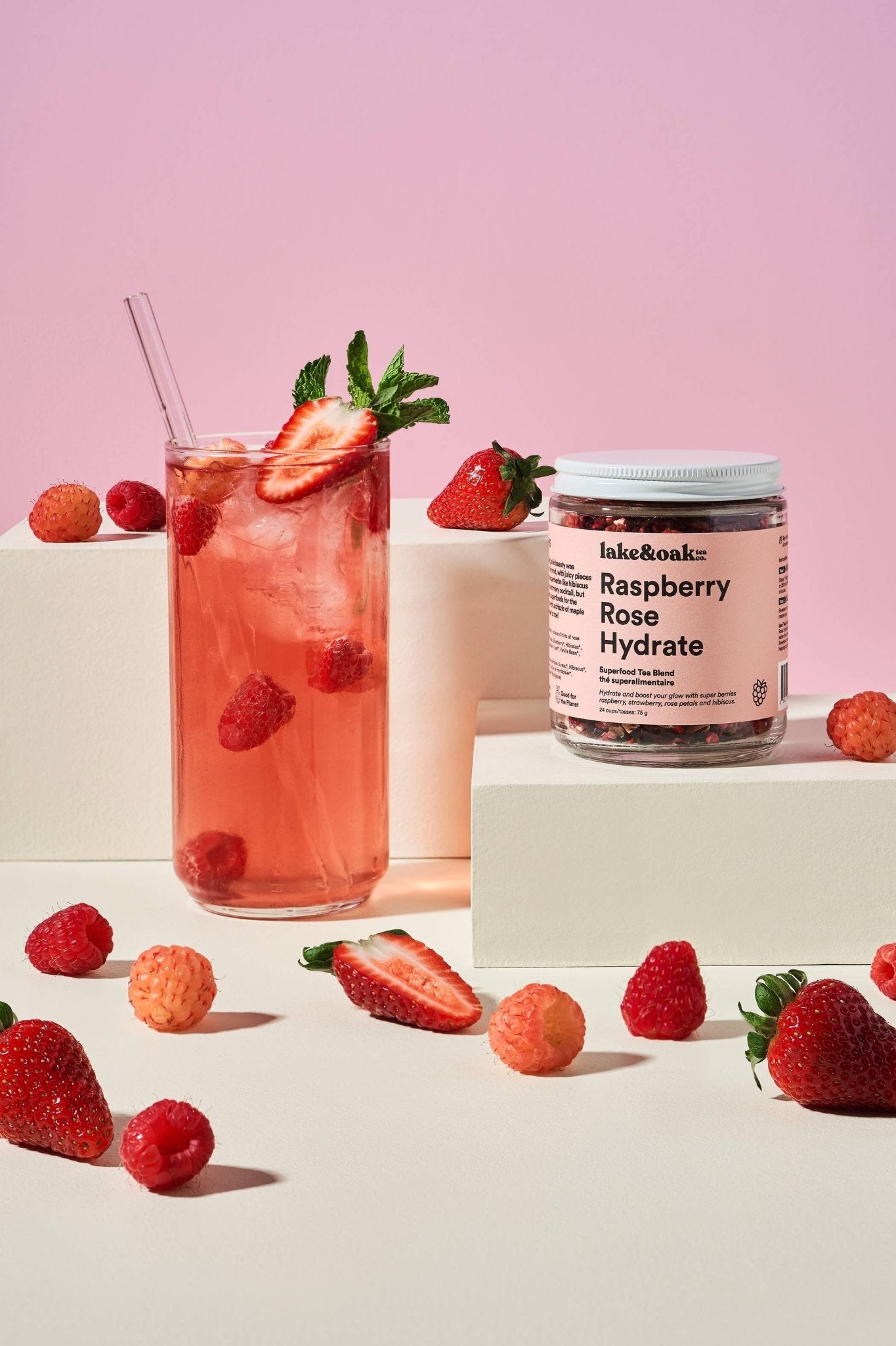 Glass of raspberry rose hydrate drink with a jar of the product on a pink background