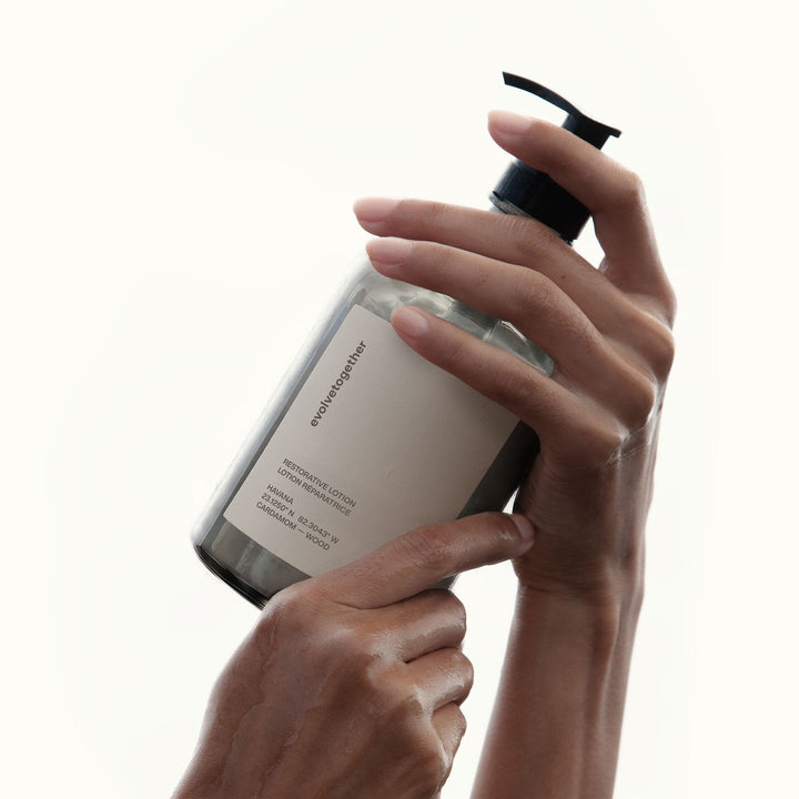 Hand holding a evolvetogether restorative lotion with a pump on a white background
