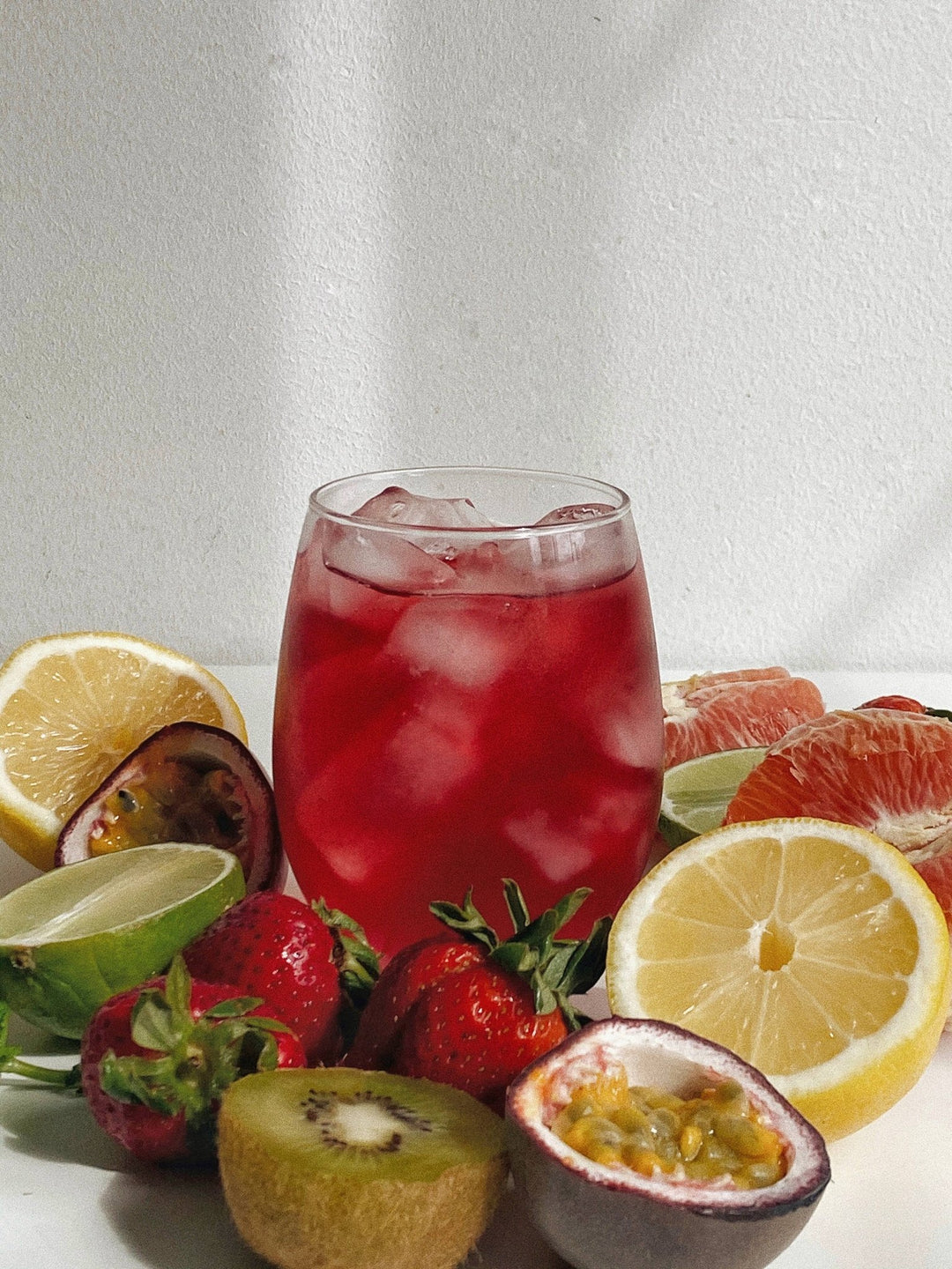 Glass of red juice with ice, surrounded by fruits on a white background