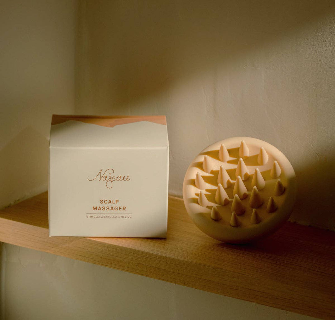 Scalp massager and packaging on a wooden shelf with a neutral background