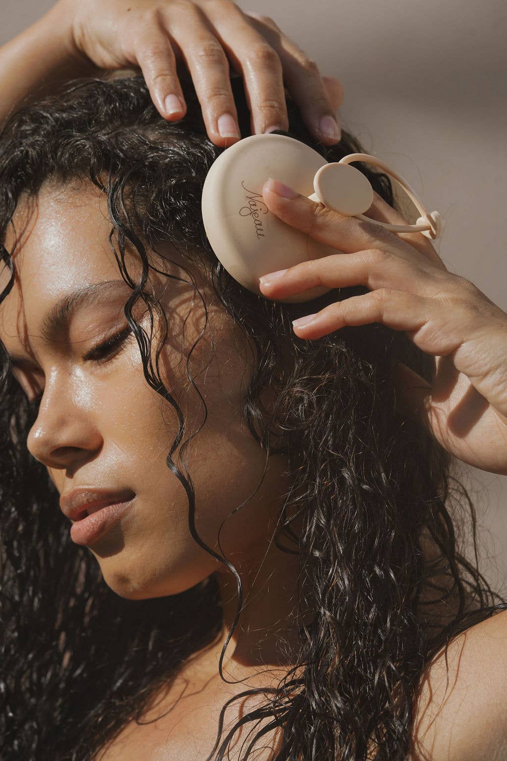Person using a scalp massager on wet hair with a neutral background