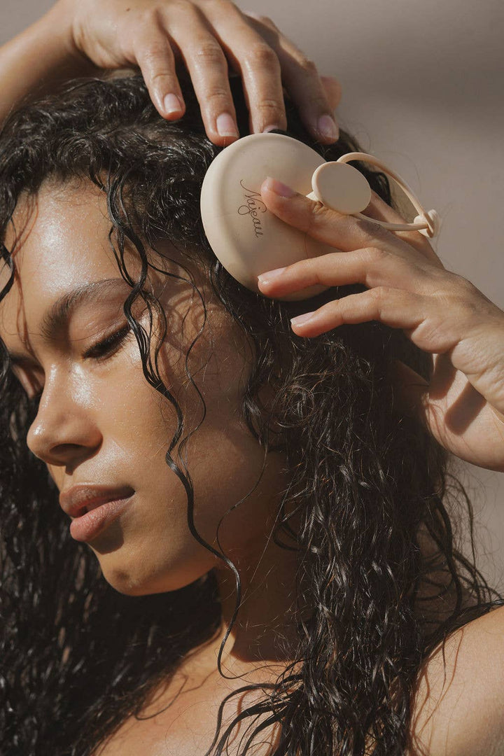 Person using a scalp massager on wet hair with a neutral background