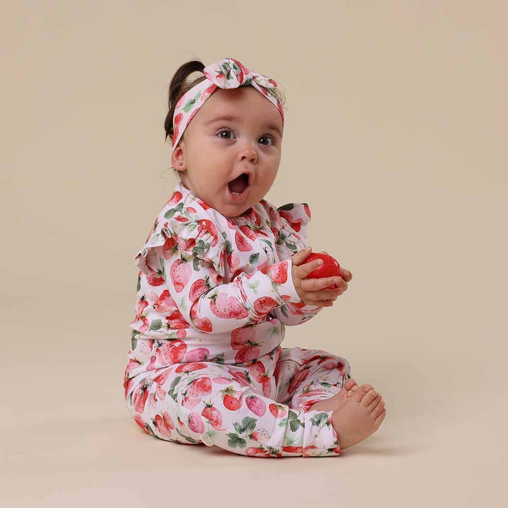 Baby wearing  Strawberry Organic Snugglesuit Convertible Romper
with a matching headband on a beige background