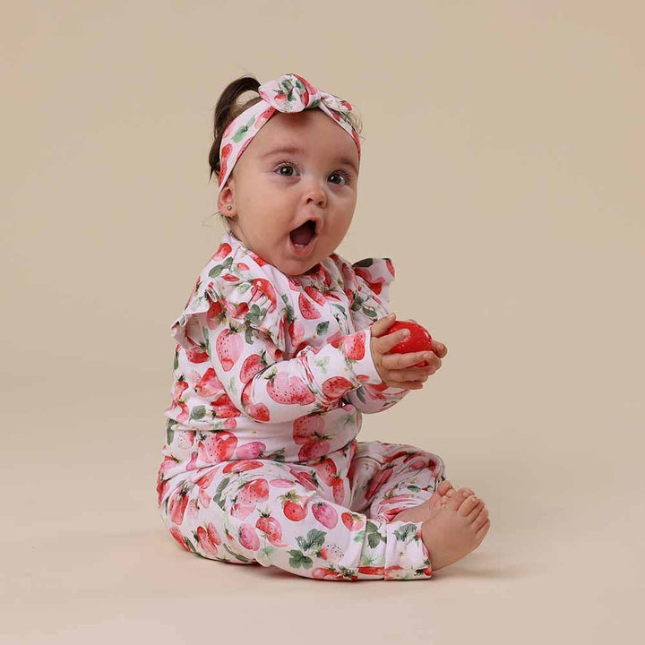 Baby wearing  Strawberry Organic Snugglesuit Convertible Romper
with a matching headband on a beige background