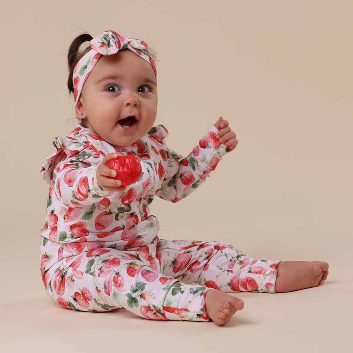 Baby wearing  Strawberry Organic Snugglesuit Convertible Romper
with a matching headband on a beige background