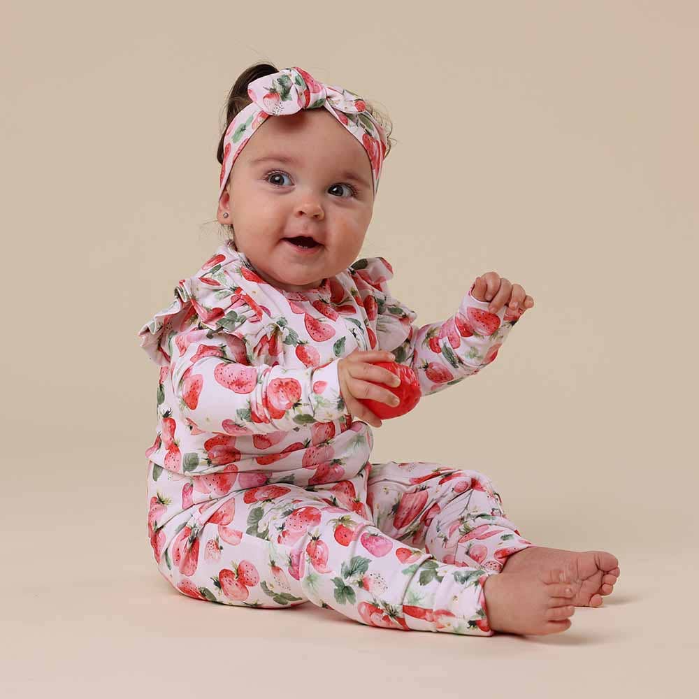 Baby wearing  Strawberry Organic Snugglesuit Convertible Romper
with a matching headband on a beige background
