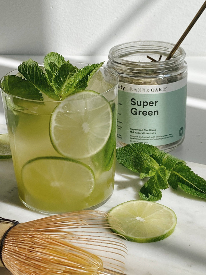 Green drink with lime slices and mint leaves next to a jar labeled &