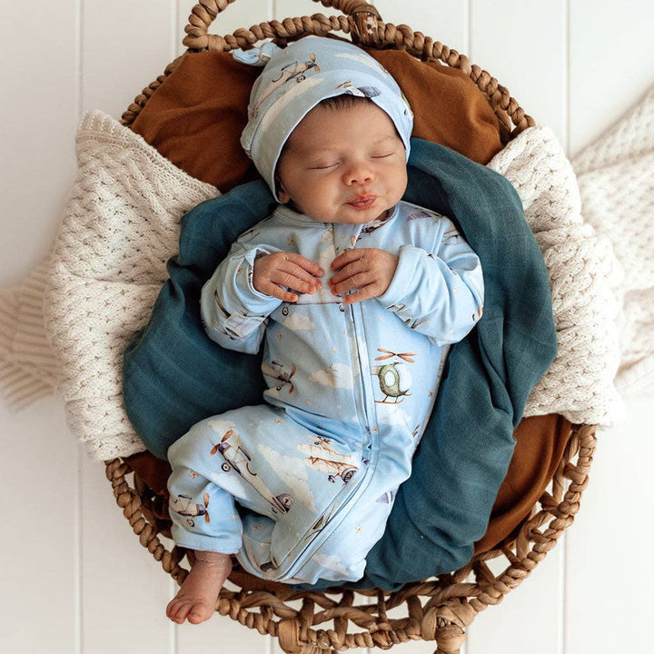 Newborn baby in a Taking Flight Organic Snugglesuit Convertible Romper, sleeping in a woven basket.
