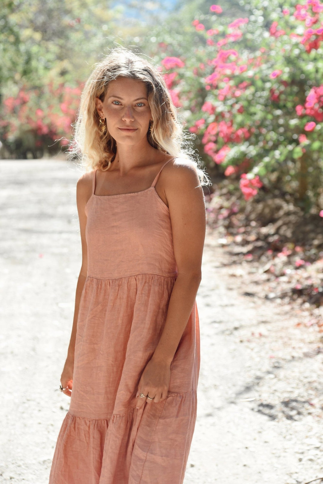 Woman in a pink dress standing in a garden with pink flowers and greenery.