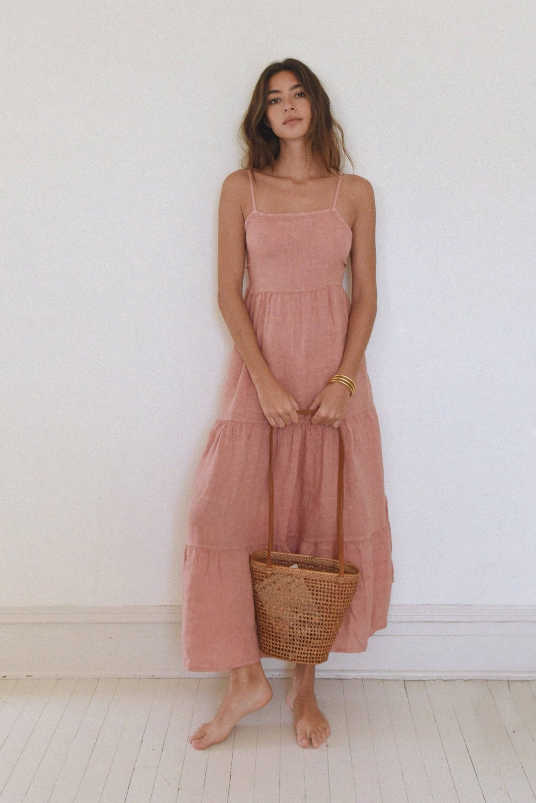 Woman wearing a pink dress holding a woven basket against a white wall.