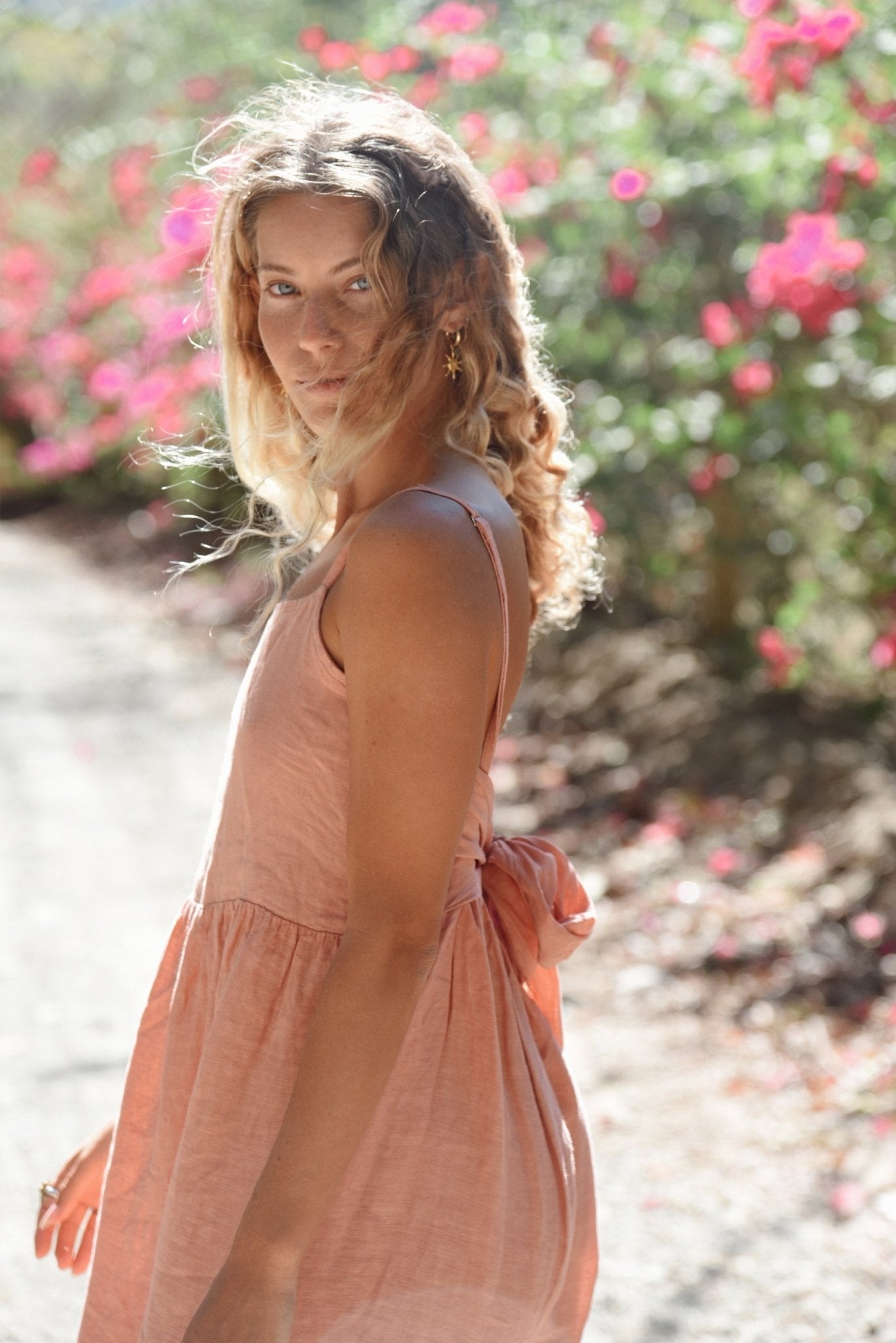 Woman in a pink dress standing outdoors with flowers in the background