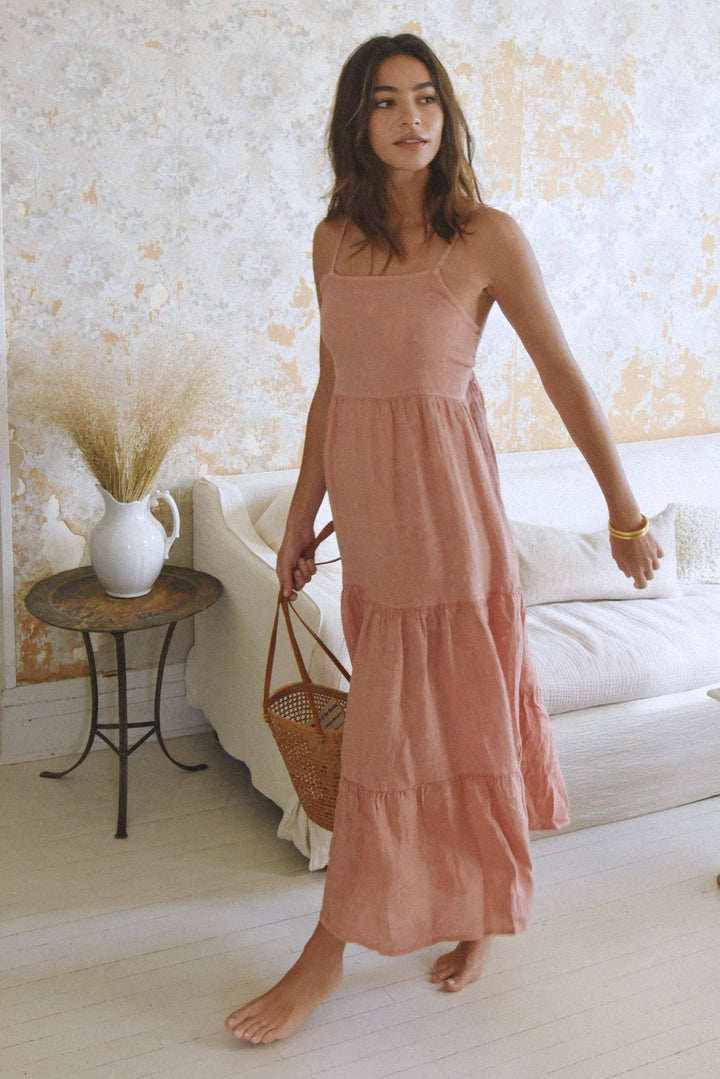 Woman in a long pink dress standing in a room with a textured wall and a small table.