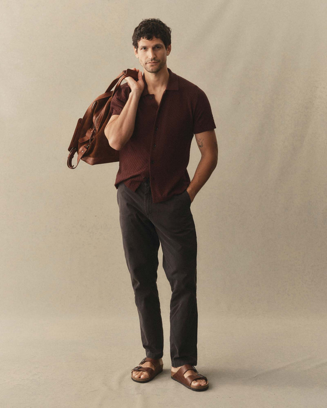 Man holding a bag over his shoulder wearing The Arlo Sweater Polo
in Burgundy Texture Knit against a plain background