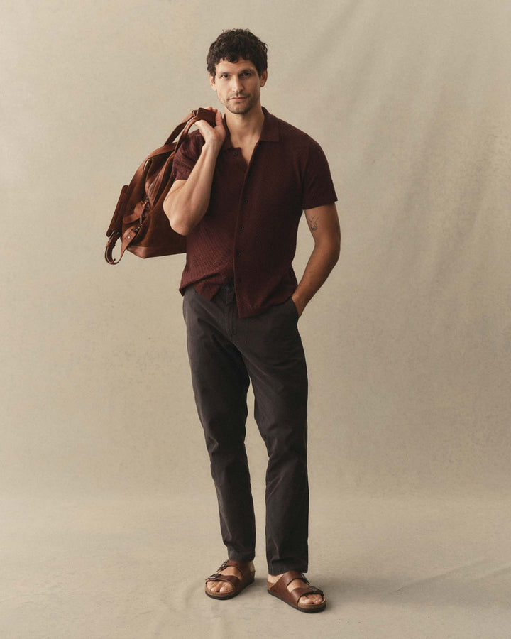 Man holding a bag over his shoulder wearing The Arlo Sweater Polo
in Burgundy Texture Knit against a plain background