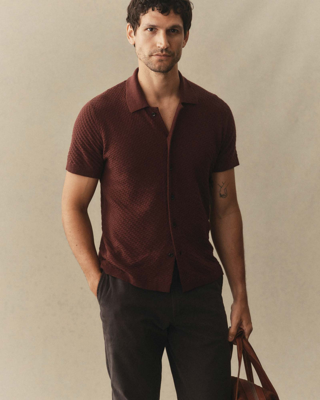 Man wearing The Arlo Sweater Polo
in Burgundy Texture Knit and dark pants against a beige background