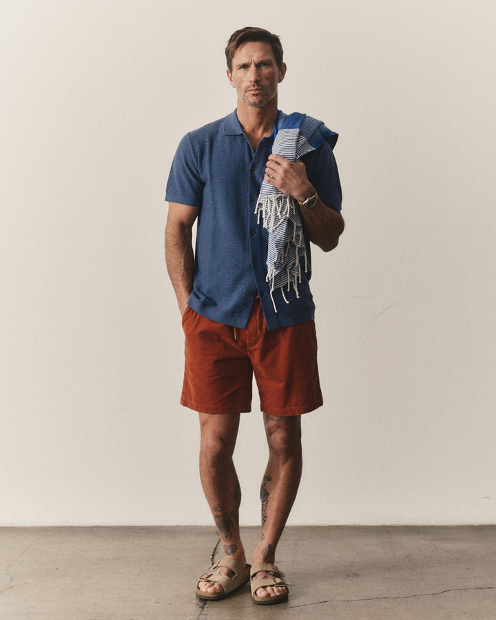 Man wearing a Taylor Stitch Button Down Polo in Gulf Stream Herringbone with red shorts with a beige background
