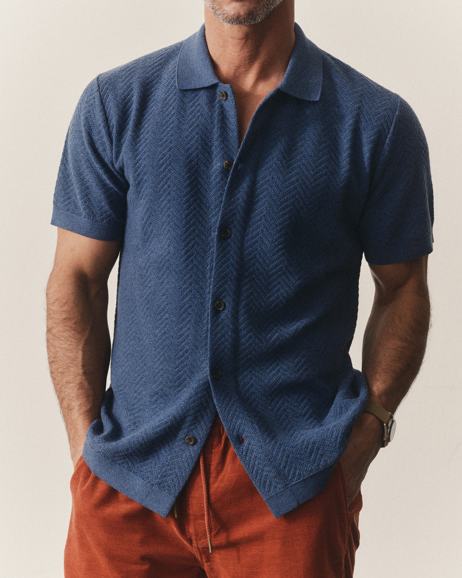 Man wearing a Taylor Stitch Button Down Polo in Gulf Stream Herringbone with red shorts with a beige background