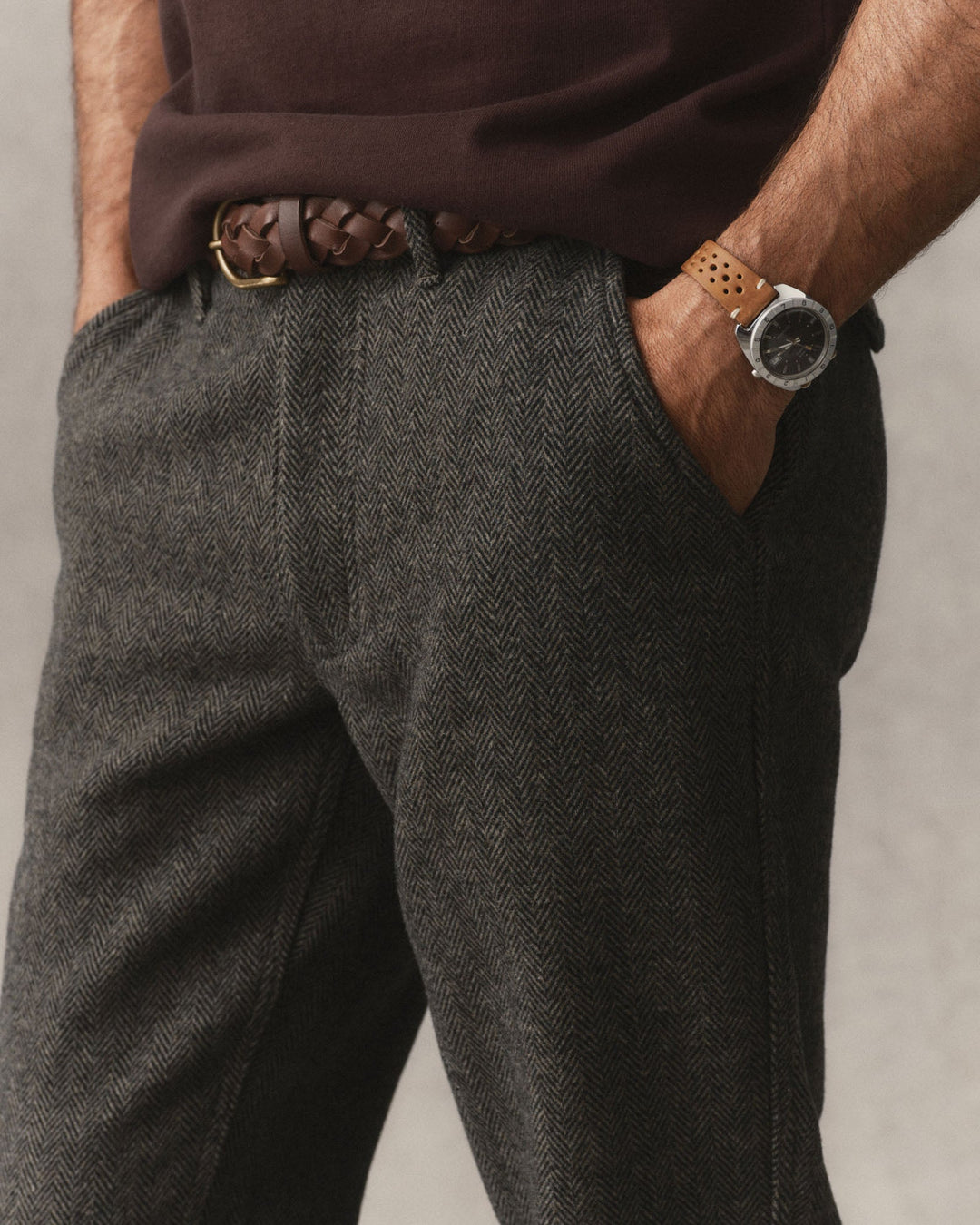 A close-up of The Carnegie Pant
in Walnut Herringbone Wool, styled with a brown braided leather belt, a dark brown shirt, and a brown leather watch strap.