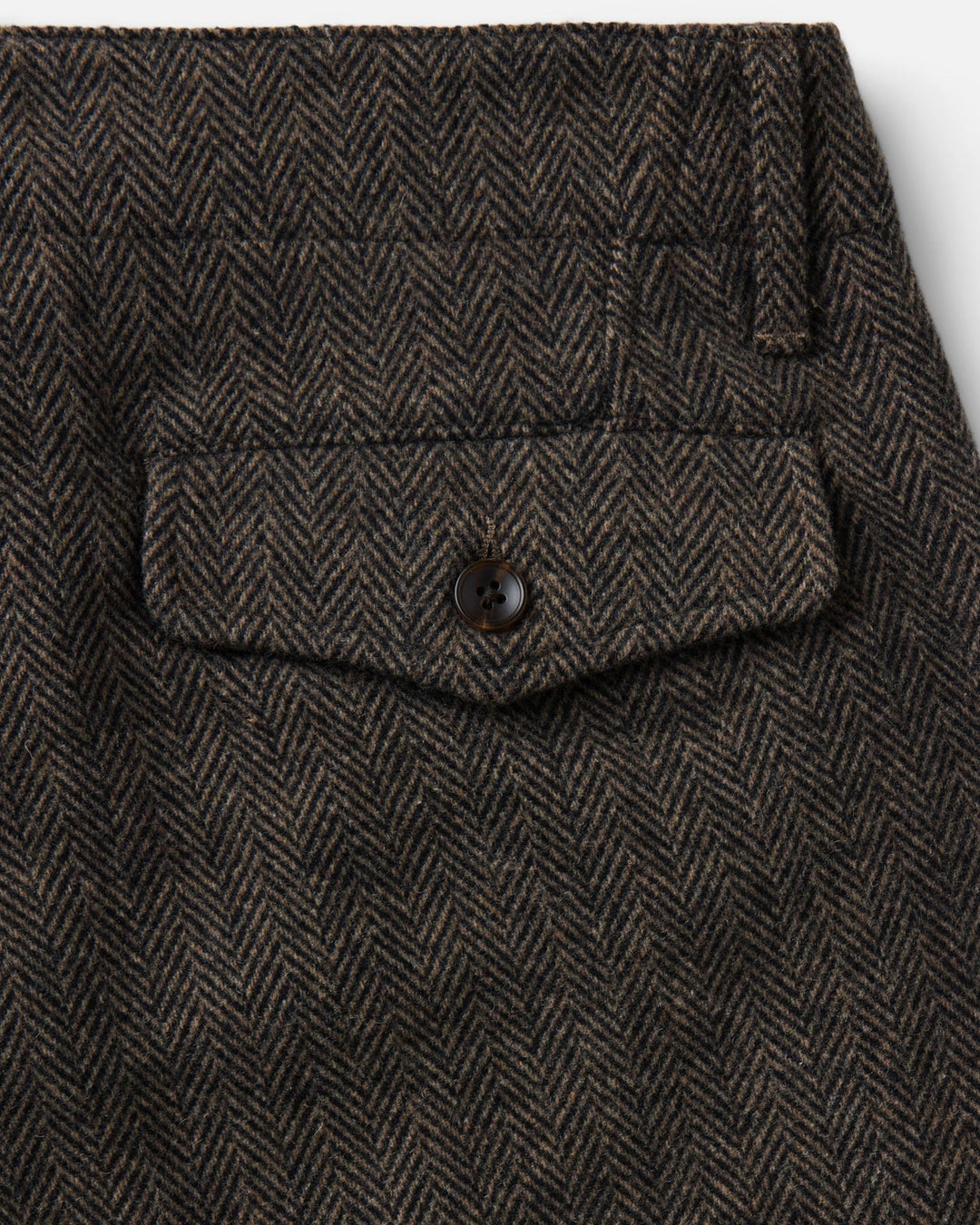 Close-up of The Carnegie Pant
in Walnut Herringbone Wool, showing a buttoned flap pocket and belt loop details.