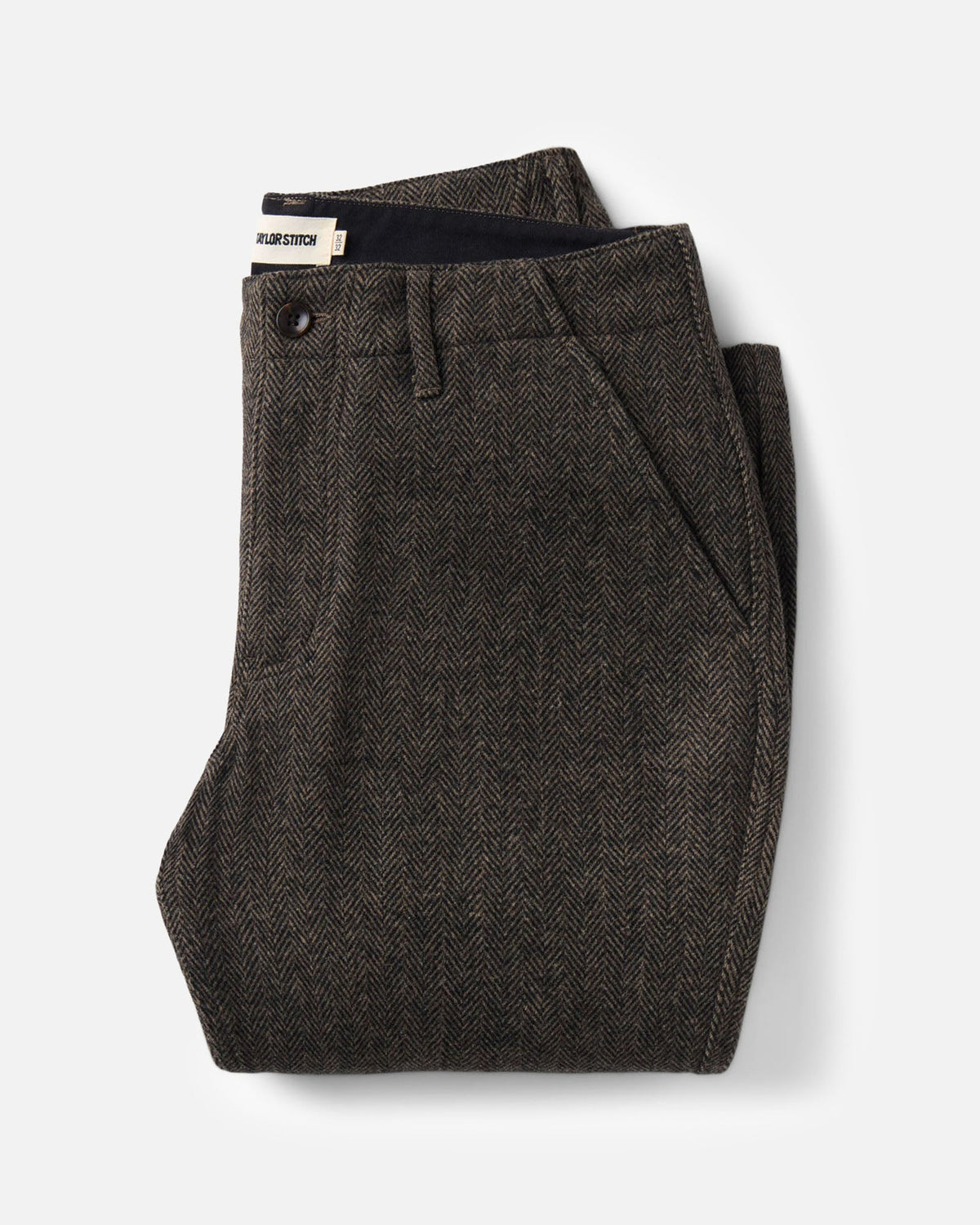 A pair of folded Carnegie Pants
in Walnut Herringbone Wool with a black button and waistband, displayed on a clean light gray background.