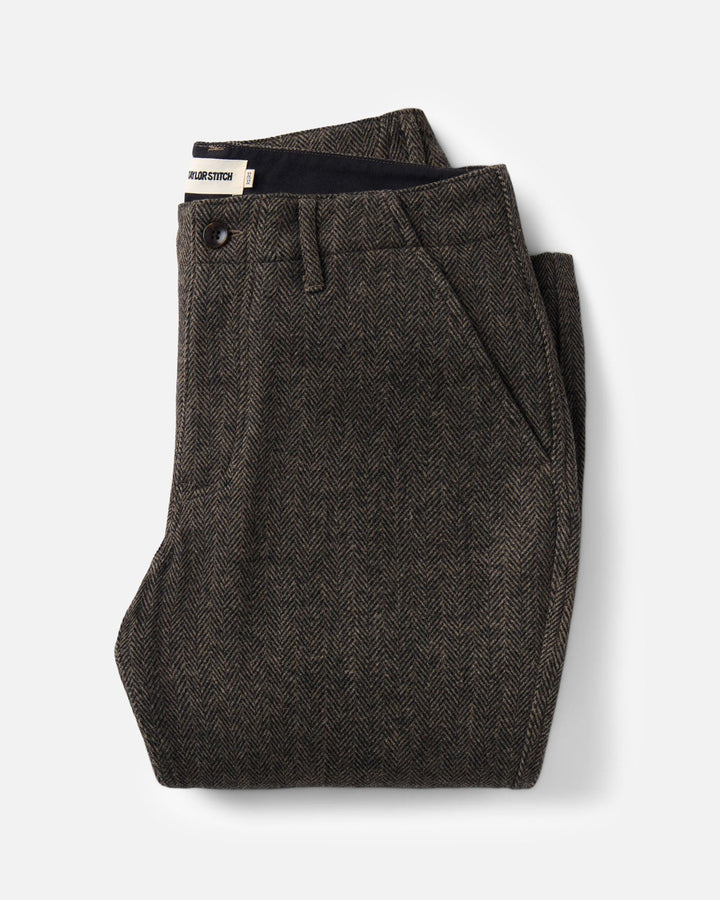 A pair of folded Carnegie Pants
in Walnut Herringbone Wool with a black button and waistband, displayed on a clean light gray background.