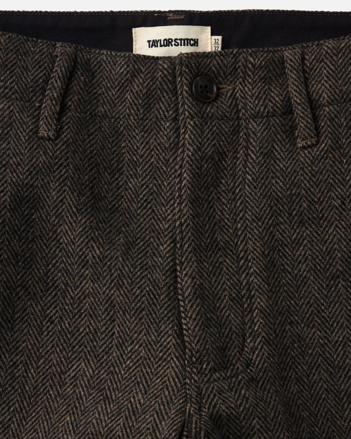 Close-up of a pair of The Carnegie pants
in Walnut Herringbone Wool showing the waistband, button, belt loops, and a visible Taylor Stitch brand label.