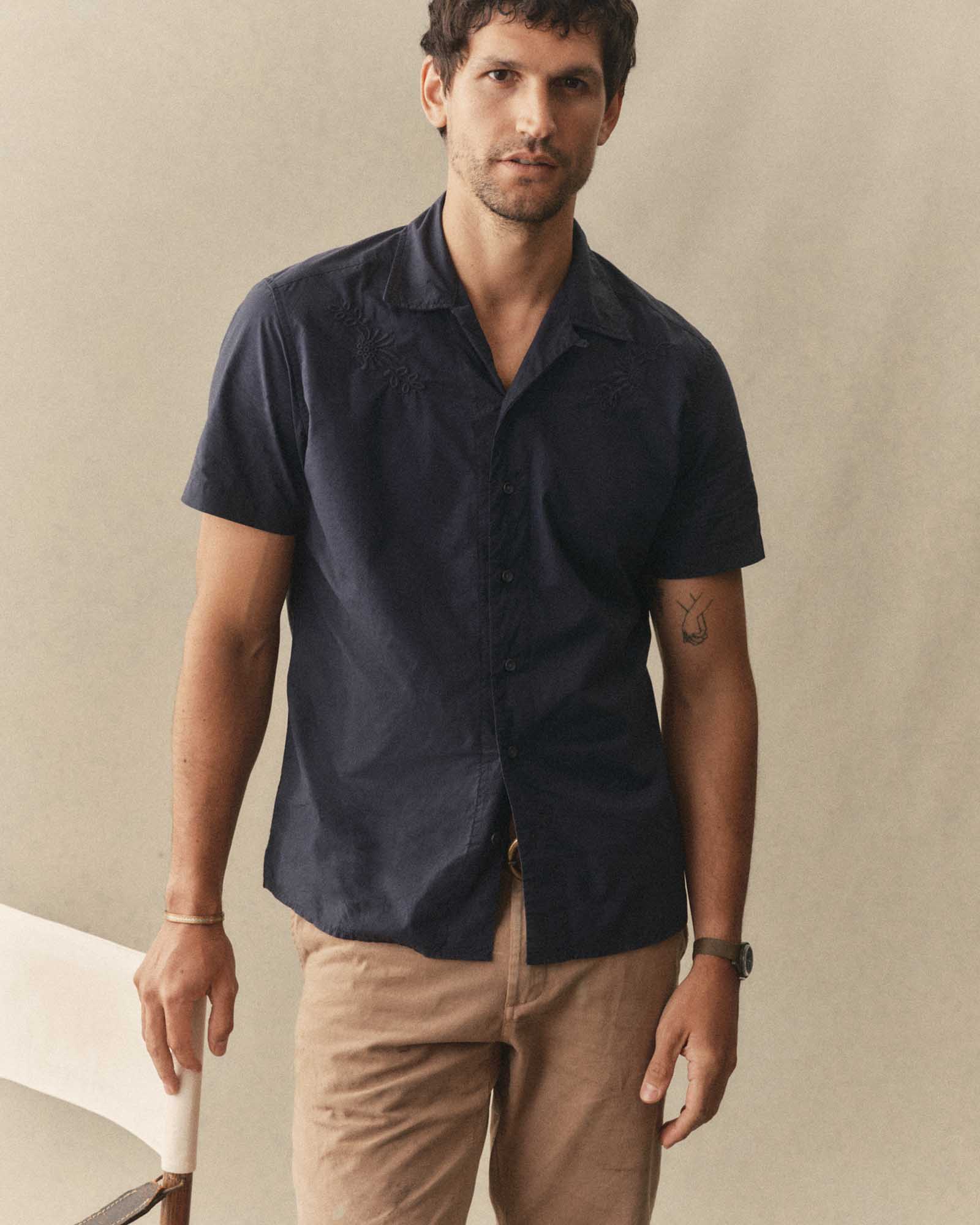 Man wearing The Davis Shirt in Navy Floral Embroidery and beige pants against a beige background