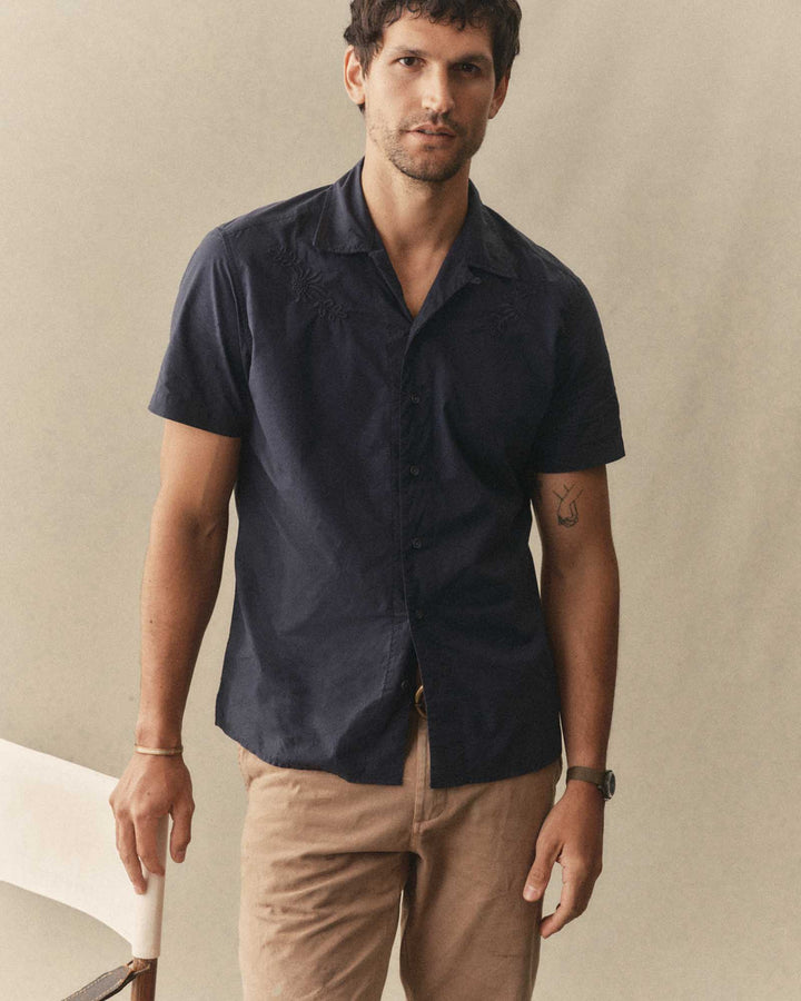 Man wearing The Davis Shirt in Navy Floral Embroidery and beige pants against a beige background