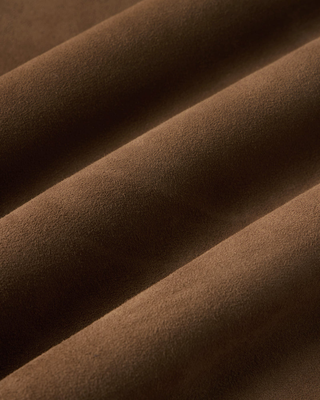 A close-up of draped brown suede fabric with soft folds and a matte texture.