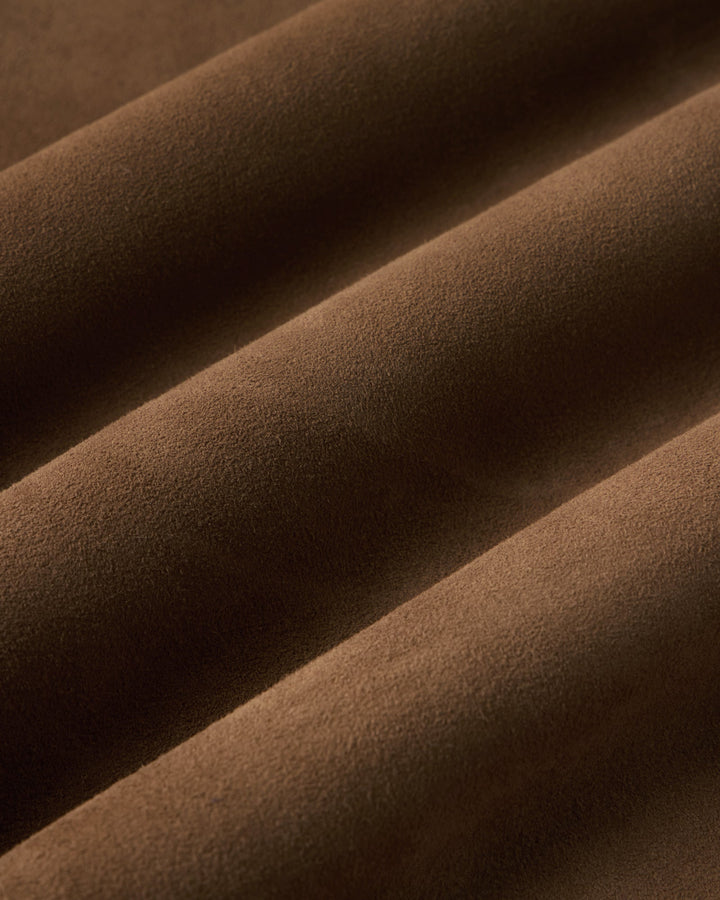 A close-up of draped brown suede fabric with soft folds and a matte texture.